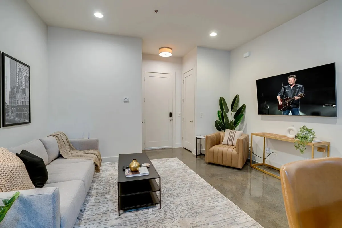 A comfortable living room centered around a sofa facing a flat-screen television, with a coffee table and decorative plant. The space is ideal for movie nights, watching favorite shows, or simply relaxing after a busy day.