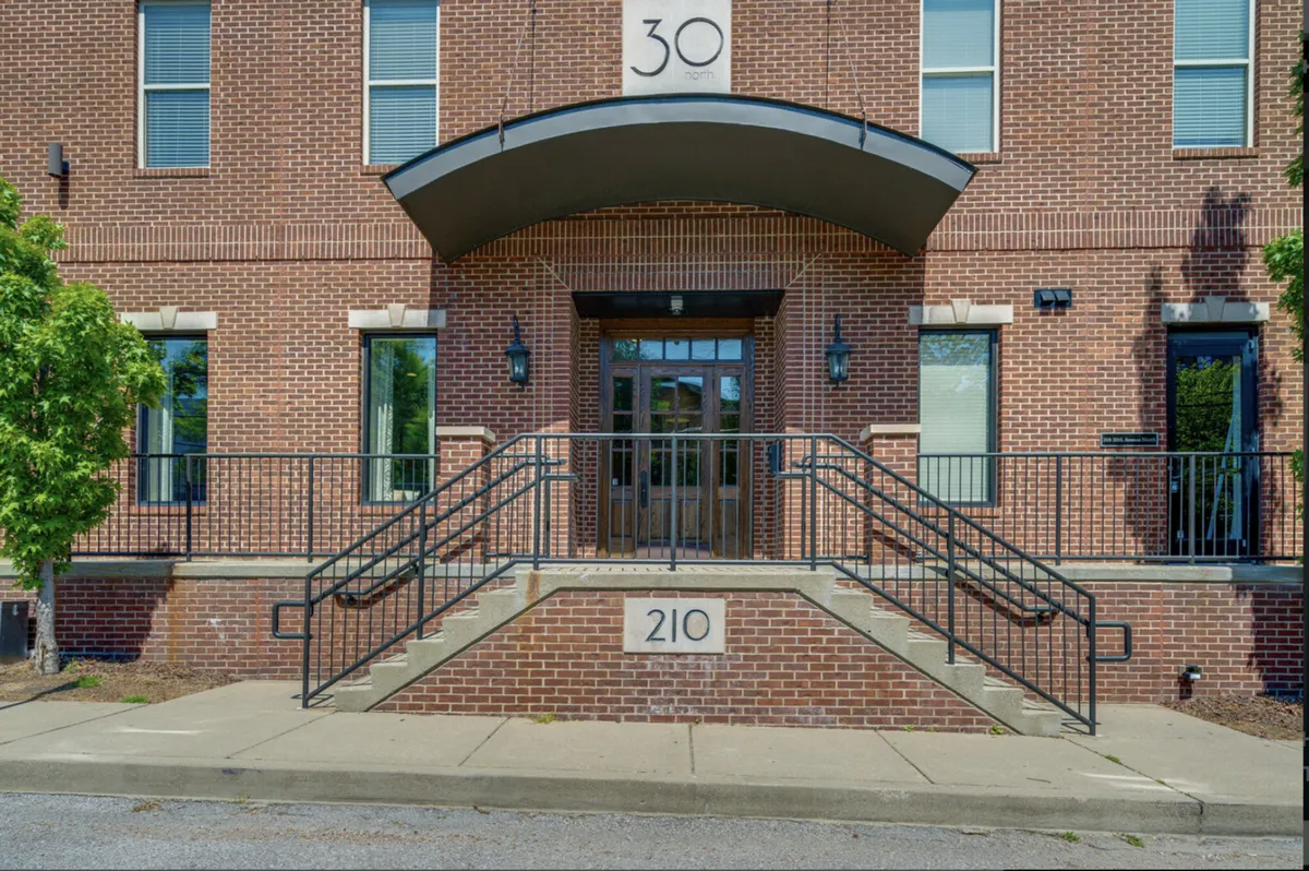 The main entrance of a brick-faced residential building with a visible staircase and signage. The entryway is well-lit, hinting at security and professionalism, while also being inviting for families arriving for their stay.