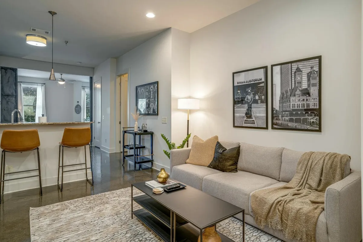 A bright, open-plan living area that features a sofa, stylish artwork, a kitchen island with bar stools, and a welcoming ambiance. The blend of lounging and dining space highlights flexibility for both relaxation and entertaining guests.