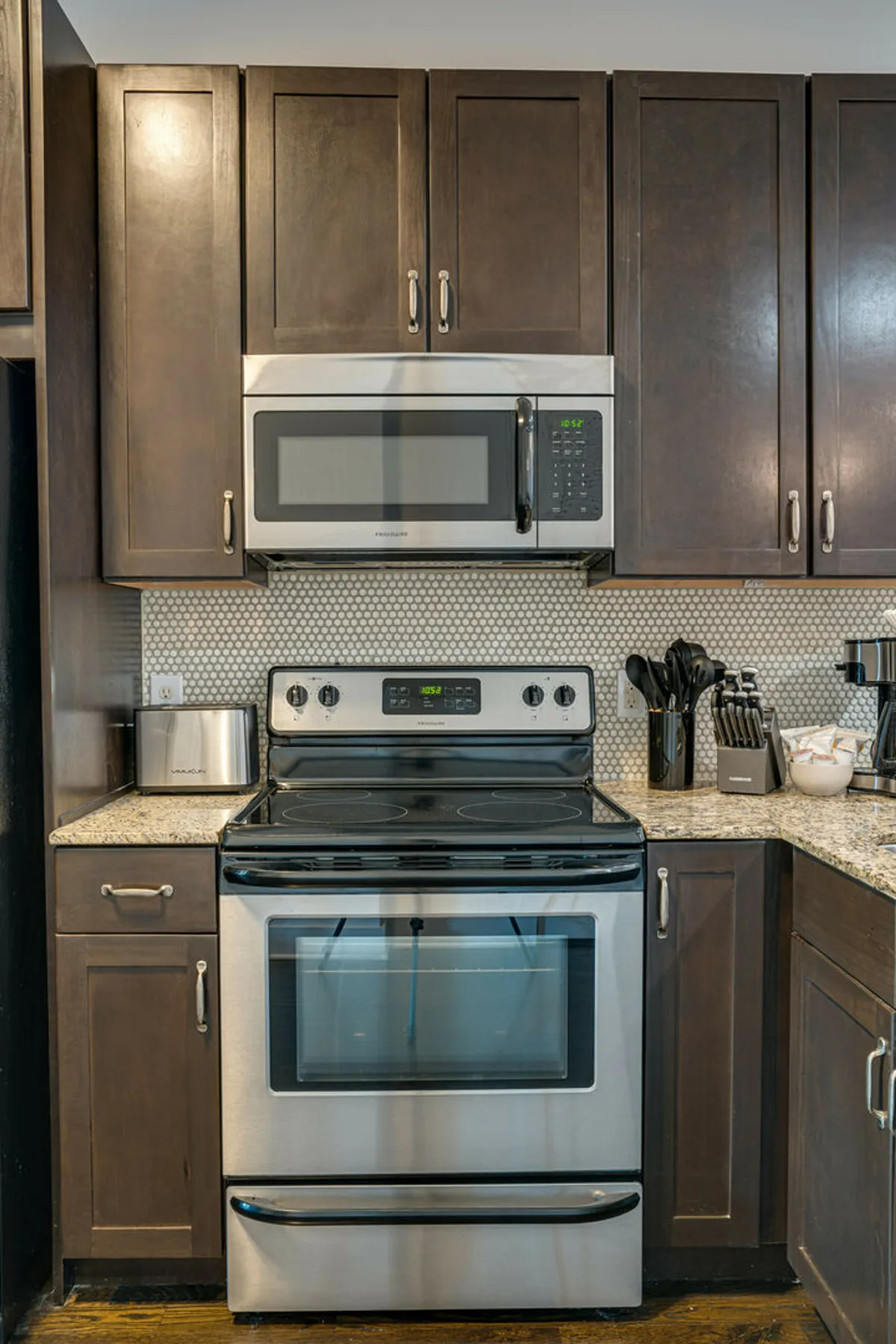 A modern kitchen with stainless steel stove and microwave, granite countertops, and a textured backsplash. The scene is inviting and practical, with visible space for baking, cooking, and meal preparation.