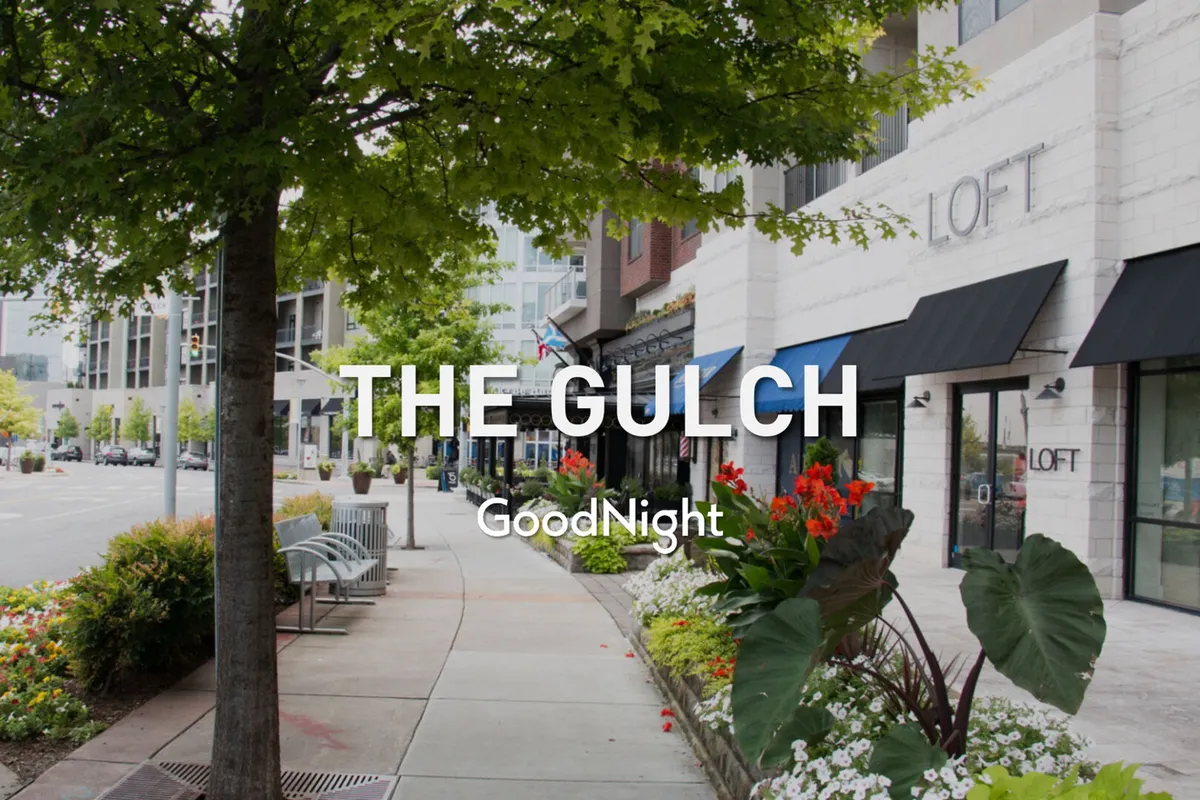 A lively pedestrian street scene with trees, flowers, benches, and attractive storefronts. People are seen strolling and socializing, and the area feels safe and inviting for families looking to explore nearby dining and retail options.